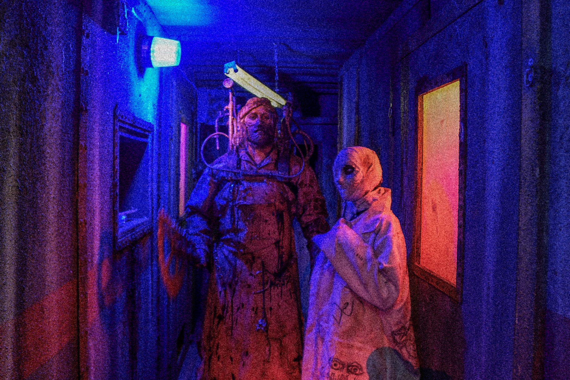 Two disfigured actors in a blue and red lit hallway