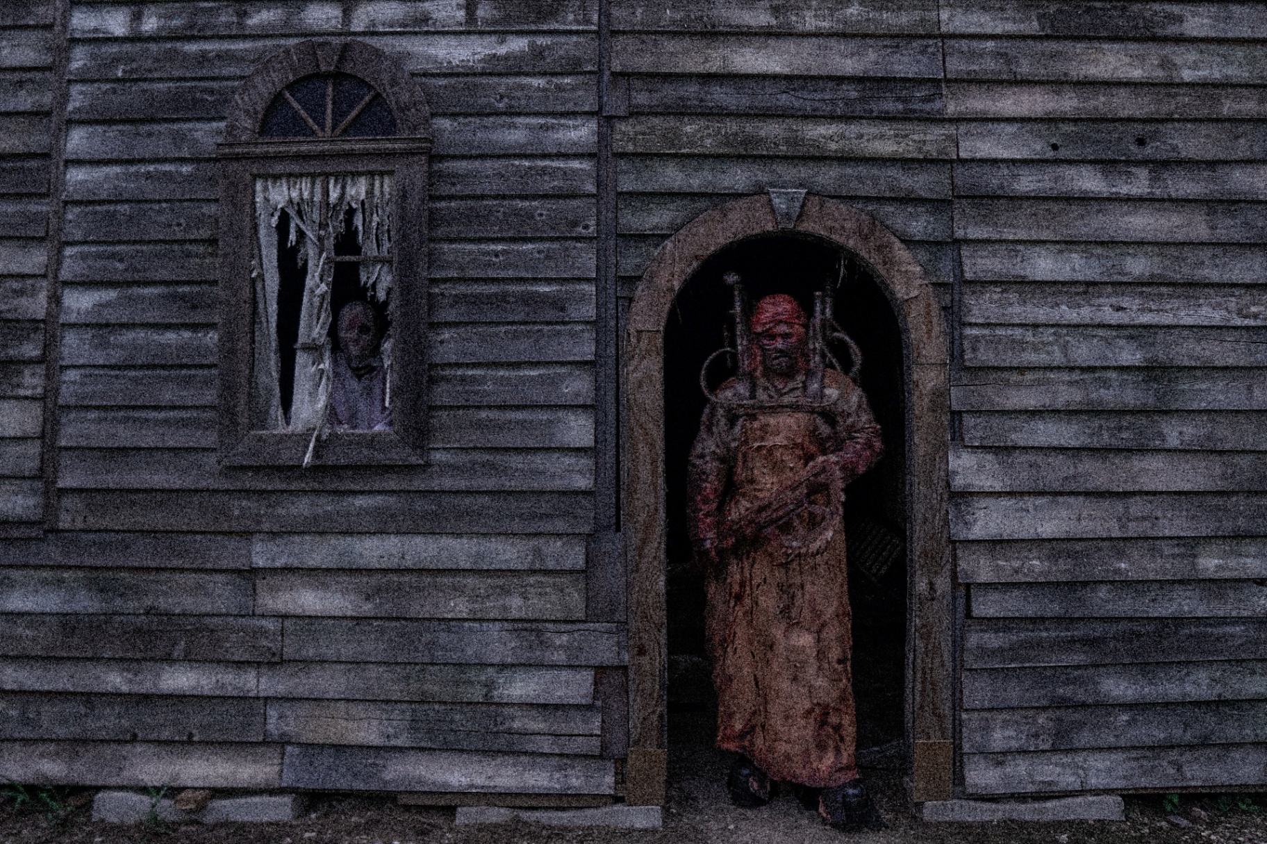 Bloodied figure in doorway of weathered building with second figure in window